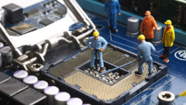 Miniature figurines, dressed as construction workers, inside a computer case working on the CPU socket.