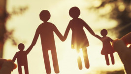 A shadow image of a paper cut-out of a man, woman, boy, and a girl holding hands.